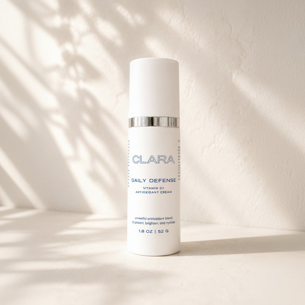 A white cylindrical skincare bottle labeled CLARA Daily Defense Vitamin E Antioxidant Cream, standing on a light surface against a textured wall with soft leafy shadows.
