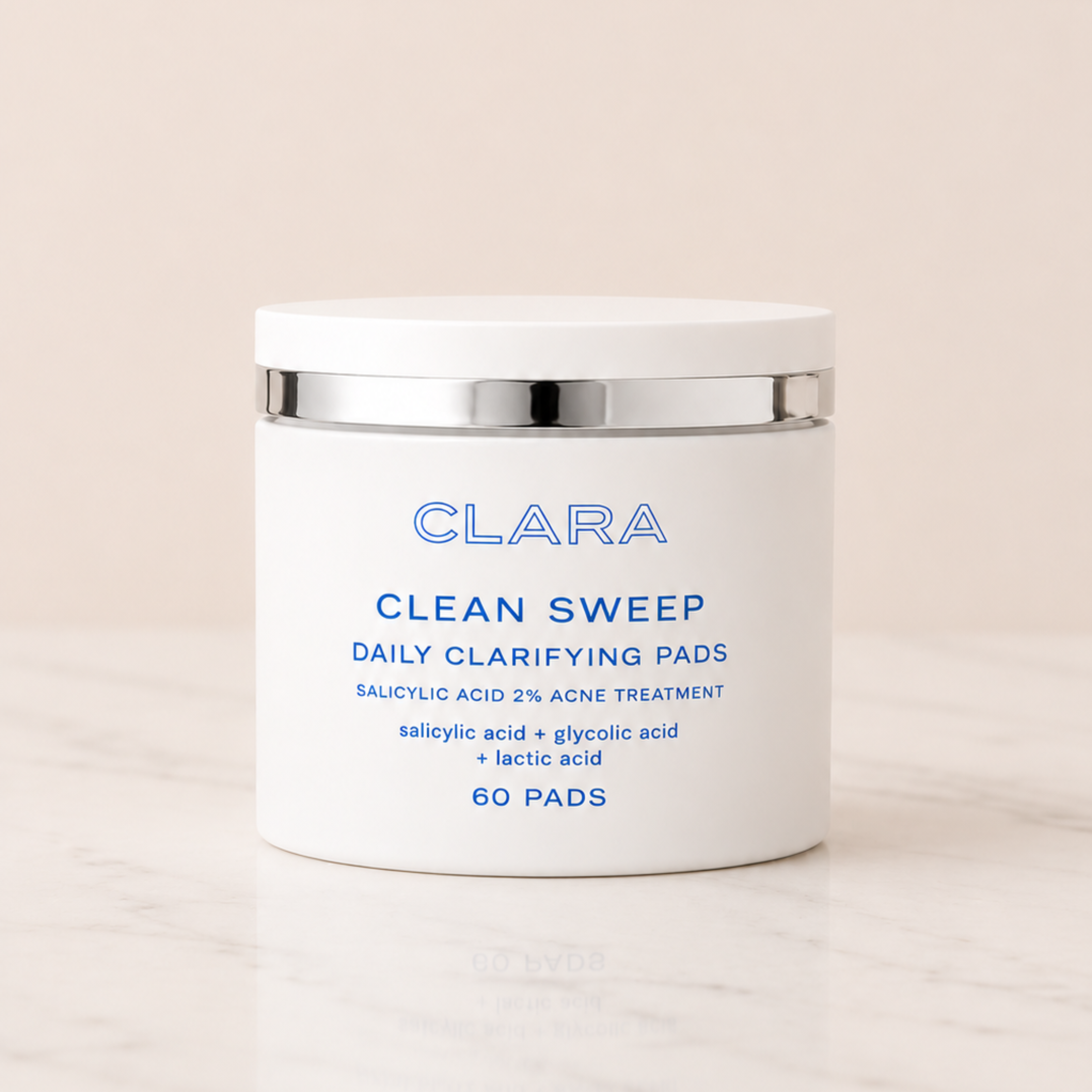 A white jar of CLARA Clean Sweep Daily Clarifying Pads with a silver metallic band and blue text, set against a warm beige background on a light marble surface.
