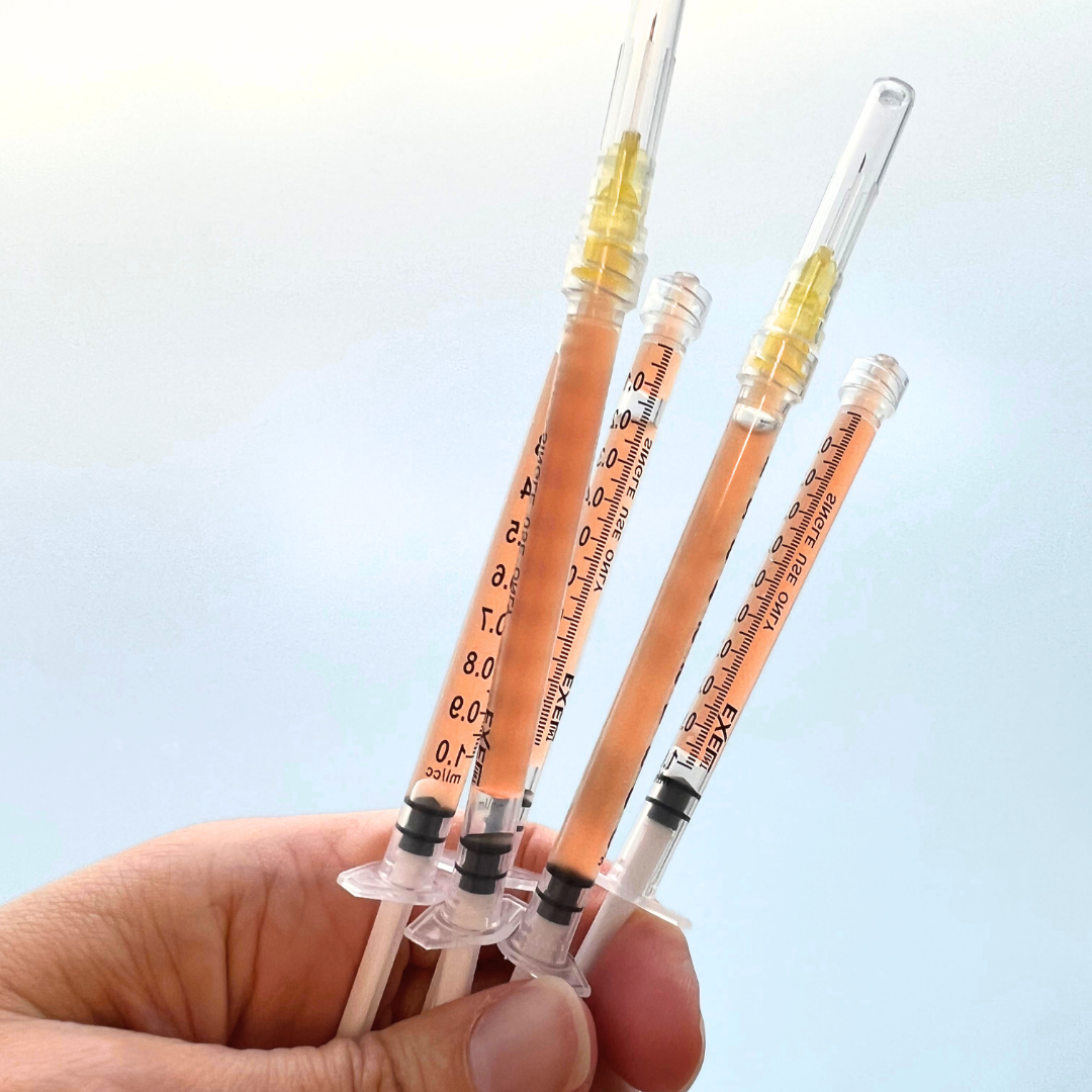 Hand holding multiple syringes with needles against a light blue background